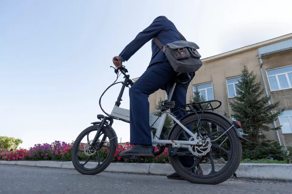 Person on folding electric bike wearing messenger bag resting foot on ground on urban street.